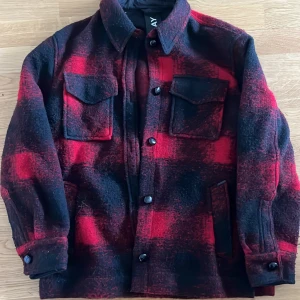 Rutig overshirt från Replay i ull - Säljer en röd och svart rutig overshirt från Replay i ullmix. Jackan har två bröstfickor med lock, knäppning framtill och klassisk krage. Perfekt lager-på-lager-plagg med snygg streetkänsla.