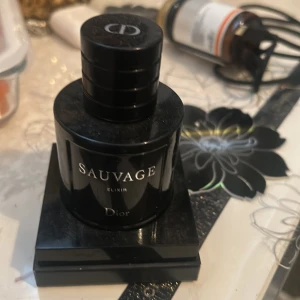 Dior Sauvage Elixir parfym - Dior Sauvage Elixir är en lyxig herrparfym i en elegant, mörkblå nästan svart glasflaska med silverfärgad text. Flaskan har en rund form och ett robust lock med Dior-loggan på toppen. Perfekt för dig som gillar exklusiva och intensiva dofter. Mer än 80% kvar på den nästan helt ny 