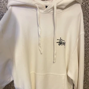  Stüssy hoodie  - Vit hoodie från Stüssy i storlek small med svart logga tryckt på bröstet och stor logga på ryggen. Klassisk huva med snörning och känguruficka framtill. Stor i storleken, passar även M. Aldrig använd, som ny!!