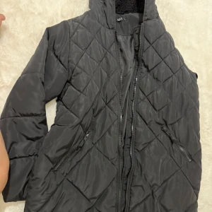 Svart quiltad lång pufferjacka - Svart lång pufferjacka från NA-KD med quiltat mönster och dragkedja framtill. Jackan har hög krage, två snedställda fickor med dragkedja och är perfekt för kyliga dagar. Snygg och stilren design som håller dig varm hela vintern.