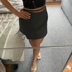 Svart kortkjol AVORA - Kortkjol med stilren design och liten slits på sidan. Kjolen har en enkel, rak passform och är perfekt att matcha med crop tops eller snygga sandaler. Materialet känns lätt och passar bra för varmare dagar. Ord pris 1599kr, aldrig använd