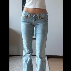 Lågmidjade True Religon jeans - Sjukt snygga ljusblå Lågmidjade jeans. Snygga slitningar och Utsydda. Innerbenslängden är 84 cm och midjemåttet tvärsöver är 36 cm. Jeansen passar någon med storlek xs.
