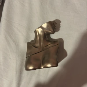 Billie Eilish Eilish Eau de Parfum - Parfymflaska i metallisk guld, formad som en byst med hals och ansikte. Flaskan har en unik och konstnärlig design med Billie Eilishs signatur ingraverad. Perfekt för dig som gillar snygga och annorlunda parfymflaskor.  Använd 10 gånger 