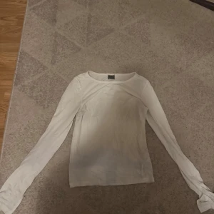 Vit långärmad tröja från Divided - En basic vit långärmad tröja från Gina Tricot med rund halsringning. Tröjan är i mjuk bomull och har en enkel, slim passform som funkar till allt. Perfekt att styla med jeans eller kjol för en clean look. Den har utsvängda armar med slits på vardera arm