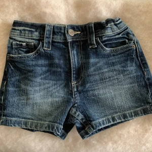 Mörkblå jeansshorts från H&M - Snygga mörkblå jeansshorts från H&M med klassisk femficksdesign, justerbar midja och olika detaljer som silvriga knappar. De är oanvända och helt nya med lappen kvar. Gjorda i denim med 20% återvunnen bomull. Perfekta för sommardagar och enkel att matcha med allt. 