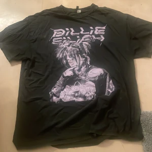 Billie Eilish svart t-shirt H&M M - Svart t-shirt med stor tryckt Billie Eilish-grafik i lila på framsidan. Klassisk rund hals och korta ärmar. Materialet är mjuk bomull, perfekt för dig som gillar streetstyle och vill sticka ut med en cool artisttröja.