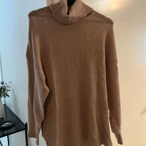 Beige stickad polotröja - Mysig beige stickad polotröja med oversized passform och långa ärmar. Tröjan har en hög, ribbad polokrage och är tillverkad i ett mjukt material som passar perfekt för kyliga dagar. OBS! Ett hål finns vid högt upp på vänsteraxel men polon kan gömma/täcka hålet