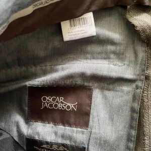 Grå kostymbyxor från Oscar Jacobson - Snygga grå kostymbyxor från Oscar Jacobson i klassisk rak modell. Byxorna har diskreta fickor i sidorna och är tillverkade i ett fint vävt material som ger en stilren look. Perfekta för dig som vill ha en clean och dressad stil.