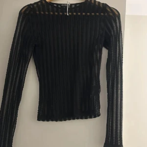 Svart festtopp  - Säljer en oanvänd svart långärmad topp från monki med transparenta ränder. Toppen är figurnära och har en cool, modern look med rund hals. Perfekt till vardag, fester men även högtider som nyår! Hör gärna av er vid intresse, pris går att diskuteras vid snabb affär! 