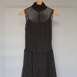 Svart prickig ärmlös klänning med spets, COMME CA ISM - Supersöt svart ärmlös klänning med vita prickar, hög rynkad krage och transparent mesh upptill. Kjolen är lätt utställd och avslutas med spetsdetaljer. Perfekt för dig som gillar en feminin och trendig look. (Storleken på etiketten är L, men det är ett japanskt märke, så den passar mer som M)