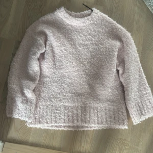 Ljusrosa fluffig stickad tröja - Supermjuk och fluffig ljusrosa stickad tröja med rund hals och långa ärmar. Perfekt för kalla dagar när du vill vara extra cozy. Tröjan har en avslappnad passform och ribbade detaljer vid nederkant och ärmslut.