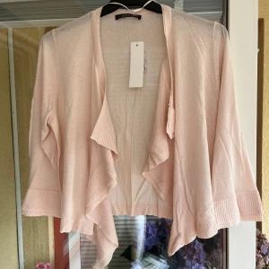 Ljusrosa kofta från Esprit - Superfin ljusrosa kofta från Esprit med öppen front och snygga volangdetaljer längs kanterna. Koftan är tunn och har långa ärmar med breda ribbade muddar. Perfekt att slänga över en topp under vår och sommar.  Storlek S/M.