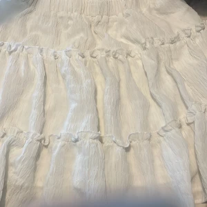 Vit volangkjol från Set You Free - Superfin vit kjol från Set You Free i storlek 36. Kjolen har flera volanglager och ett krinklat tyg som ger en luftig känsla. Perfekt för sommarens alla tillfällen och har en romantisk vibe med sina mjuka detaljer.