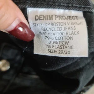Svarta straight jeans från Denim Project - Säljer ett par svarta straight fit jeans från Denim Project, modell DP Boston Straight. Jeansen är tillverkade av återvunnen bomull och har klassisk femficksdesign och knappgylf. Snyggt tvättade för en cool, lite sliten look.
