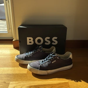 Mörkblå sneakers från BOSS, strl 42 - Snygga mörkblå sneakers från BOSS med vit sula och vita detaljer. Skorna har klassisk snörning, rund tå och är tillverkade i textil med textilfoder. Perfekta för en clean och stilren look, med diskret BOSS-logga på sidan. Ny pris är 1299. Priset går såklart diskuterad.