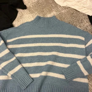 Blåvit randig stickad tröja Jessica Simpson - Supermysig stickad tröja från Jessica Simpson i ljusblått med vita ränder. Tröjan har hög krage, långa ärmar och breda ribbade muddar vid ärmslut och nederkant. Perfekt för kyliga dagar och enkel att styla med jeans eller kjol.