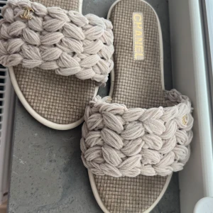 Beige sandaler, storlek 37 - Superfina beige sandaler med chunky stickad ovandel och ikonisk guldfärgad logga. Sval och mjuk känsla med vävd sula och bred rem. Perfekta för sommaren och ger en lyxig touch till din outfit.