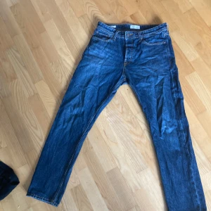 Blå jeans från Jack & Jones - Snygga blå jeans från Jack & Jones med klassisk femficksdesign och raka ben. Jeansen har en mörkblå tvätt och är tillverkade i jeansmaterial. Perfekta för en avslappnad och stilren look. Jeansenhat en liten defekt på höger knä. Som går att laga enkelt. Storlek 30.32.