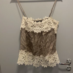 Beige linnetopp med spets från Zara - Supersöt beige linnetopp från Zara med tunna axelband och detaljerad vit spets längs både halsringning och nederkant. Toppens tyg har en lätt skrynklig struktur och ger en romantisk vibe. Perfekt att styla med jeans eller kjol nu på sommaren💘💕