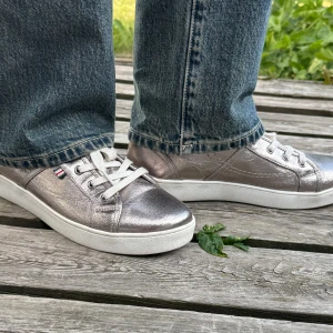 Silvriga sneakers - Snygga sneakers i metallic-silver från XIT  med vit sula och vita snören. Skorna har en låg profil och en liten logga i rött, vitt och blått på sidan. Perfekta för dig som vill sticka ut med en cool och modern look.