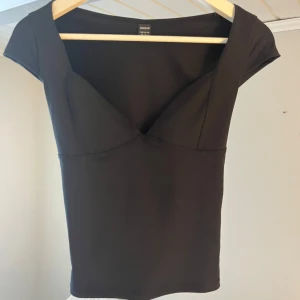 Svart topp med v-ringning från SHEIN - Snygg svart topp från SHEIN i storlek XS. Modellen har en djup v-ringning och korta ärmar, vilket ger en trendig och feminin look. Toppens material är stretchigt och figurnära, perfekt att styla med jeans eller kjol.