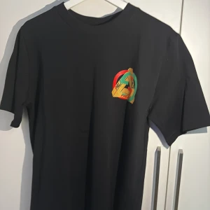 Gucci x Palace svart t-shirt M - Svart t-shirt från Gucci x Palace med stort färgglatt Palace-tryck i guld, rött och grönt på ryggen och mindre logga på bröstet. Klassisk passform och rund hals. Tillverkad i mjuk bomull, perfekt för dig som gillar streetwear och exklusiva samarbeten.