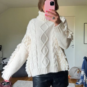 Vit stickad polotröja med fransar - Supermysig vit stickad polotröja med flätstickade detaljer och fransar längs ärmarna. Oversized passform.