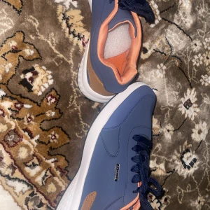 Blå finskor med orange detaljer - Snygga finskor i blått med marinblå snörning, orange foder och beige detalj vid hälen.Perfekta för dig som vill ha en fräsch och modern look. Sprillans nya aldrig använda, köptes 1 månad sen för 430kr och passade ej.