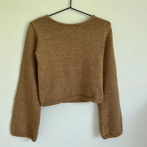 Beige/brun stickad tröja med öppen rygg  - Superfin beige/brun stickad tröja från Indiska  i storlek XS. Tröjan har lång ärm, croppad passform och en snygg öppen ryggdetalj som gör den extra trendig. Perfekt att styla med jeans eller kjol för en chill look.
