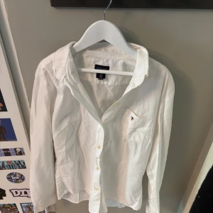 Vit skjorta från Gant  - Klassisk vit skjorta från Gant i mjuk bomull. Skjortan har lång ärm, knappar framtill och en bröstficka med liten broderad logga. Perfekt för en clean och stilren look. Snygg passform och tidlös design.