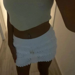 Vit spetsig minikjol med snörning - Supersöt vit kortkjol i spets med broderade detaljer och volangkant. Kjolen har elastisk midja och snörning framtill för extra snygg passform. Perfekt för sommarens alla tillfällen och ger en fräsch vibe till din outfit.