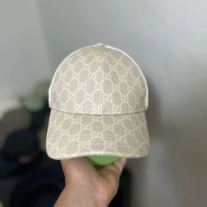 Beige Gucci keps med mesh och monogram - Snygg beige keps från Gucci med klassiskt GG-monogram över hela framsidan. Baksidan är i mesh för extra ventilation och cool vibe. Perfekt för dig som vill ha en stilren accessoar med lyxig känsla och unik personlighet. Kepsen är jätte unik inte många som har den och hade passat perfekt till vita kläder till sommaren☀️☀️