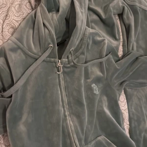 Juicy Couture velour hoodie XS - Mjuk och lyxig ljusgrön velour hoodie från Juicy Couture med dragkedja, huva och snörning. Klassisk JC-logga broderad på bröstet och stora fickor framtill. Perfekt för en chill och trendig look. Säljer båda för 1900