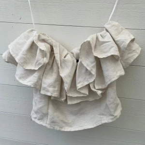 Beige volangig offshoulder topp - Superfin beige offshoulder topp med stora volanger runt hela överdelen. Dragkedja i sidan. Perfekt till sommaren. Som ny, endast använd ett fåtal gånger.