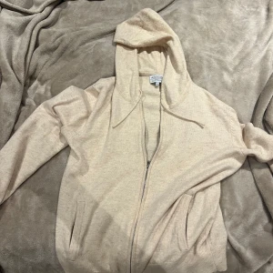 Beige hoodie från Ahlquist Clothing - Snygg beige merinoull och cashmere hoodie från Ahlquist Clothing i storlek S. Tröjan har dragkedja framtill, huva med snörning och två fickor. Mjuk och skön känsla, perfekt för chill dagar. Passar dig som gillar en enkel och stilren look. Inga defekter, använd 3-4 ggr, Köpt för 1000 mitt pris 400