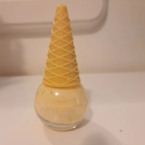 Nagellack i glasskula med strutlock - Nagellack i en rund glasflaska med ett gulligt lock som ser ut som en glasstrut. Färgen är ljusgul, nästan pastell, och flaskan rymmer 14 ml. Perfekt för dig som vill ha en söt detalj på sminkbordet och älskar unika förpackningar.