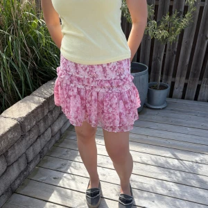 Rosa volangkjol - Kort kjol från Gina Tricot i rosa och vitt med mönster. Kjolen har smock i midjan, volanger och kan därför även användas som en bandeau topp. Storlek M men passar även S och L🌸💕