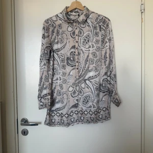 Beige paisleymönstrad skjorta med knappar - Säljer en beige/ grå skjorta med svart och grått paisleymönster. Skjortan har lång ärm, klassisk krage och knappar framtill. Materialet känns lätt och flowy, perfekt för dig som gillar unika prints och en chill vibe. Från märket Odd Molly i storlek 1 som ungefär motsvarar en storlek S. Mycket fint skick, jag hittar inga synlig anmärkningar eller defekter.  