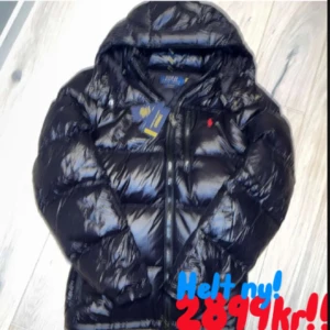 Svart glansig dunjacka Polo Ralph Lauren - Säljer en svart glansig dunjacka från Polo Ralph Lauren, modell Gorham Glossed Down Jacket. Jackan har huva, dragkedja framtill och ikonisk röd Polo-logga på bröstet. Skriv gärna för mer bilder eller liknande ( den är helt ny )