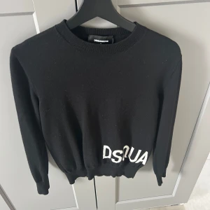 Svart stickad tröja från Dsquared2 - Svart stickad tröja från Dsquared2 med vit broderad logga 'DSQUARED2' längs nederkanten. Säljer den för att den är för liten. Tröjan är storlek S men passar XS också. Den är äkta och är som helt ny daggs finns och mycket möjligt kvitto nånstans i mina mejl. Köpt från Miinto. Ny kostar den 5000kr