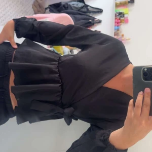 Svart omlottblus från Missay - Svart omlottblus från Missay med långa ärmar och knyt i midjan. Blusen har v-ringning och volangliknande nederdel som ger en snygg siluett. Vid funderingar eller intresse kontakta mig!🥰