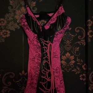 Rosa spetsklänning Seven 'til Midnight - Snygg kort rosa klänning med svarta detaljer från Seven 'til Midnight. Klänningen har blommig spets, snörning framtill och en cool v-ringning. Materialet är en mix av spets och syntet, perfekt för dig som vill sticka ut.