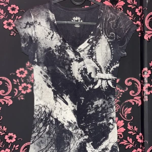 Svart och grå t-shirt från Mudd - Cool svart och grå t-shirt från Mudd med abstrakt mönster och v-ringning. Toppen har korta ärmar och är gjord i 100% bomull, vilket gör den superbekväm. Snyggt tryck framtill med en unik vibe som sticker ut.