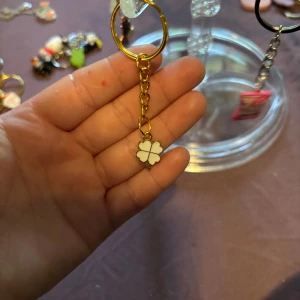 Nyckelring med vit fyrklöver - Söt nyckelring med en liten vit fyrklöver i emalj hängande på en guldfärgad kedja och ring. Perfekt accessoar för att piffa upp dina nycklar eller väska med lite extra tur och stil.