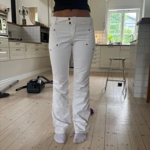 Vita lågmidjade utsvängda jeans - Snygga vita byxor från Dolce & Gabbana med utsvängda ben och låg midja. Byxorna har coola detaljer som dubbla knappar framtill, stora fickor med nitar och klassisk D&G-logga bak. Hon i bilden är 166