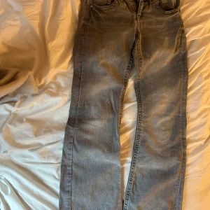 Grå jeans från Gina Tricot - Säljer ett par grå jeans från Gina Tricot i storlek 152. Jeansen är bootcut och fickor med knappar där bak