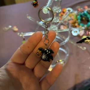 Halloweeninspirerad nyckelring med spöke - Nyckelring med ett svart spöke dekorerat med vita prickar, spindelnät och en orange pumpa. Perfekt accessoar för dig som älskar Halloween och vill ha något unikt på väskan eller nycklarna.