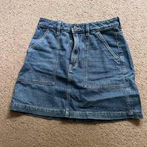 jeanskjol - Snygg blå jeanskjol med två stora framfickor och bälteshällor. Klassisk modell med knapp och dragkedja framtill. Perfekt för dig som gillar en enkel och cool stil.