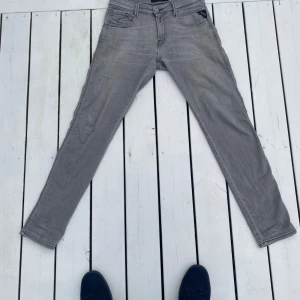 Replay Anbass grå slim jeans - Snygga grå jeans från Replay, modell Anbass med slim fit 29x32. Klassisk femficksdesign, svarta sömmar och diskret broderi på bakfickorna. Jeansen är i stretchigt denim för en bekväm passform och har dragkedjegylf. Bra skick. 