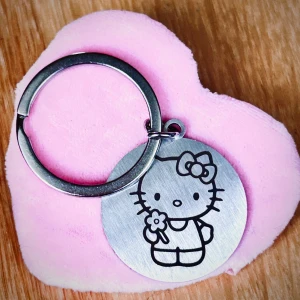 Söt nyckelring i rostfritt stål med Hello Kitty-motiv! - Söt nyckelring i rostfritt stål med Hello Kitty-motiv och peppande citat. Mått: 3 x 3 cm. Oanvänd.